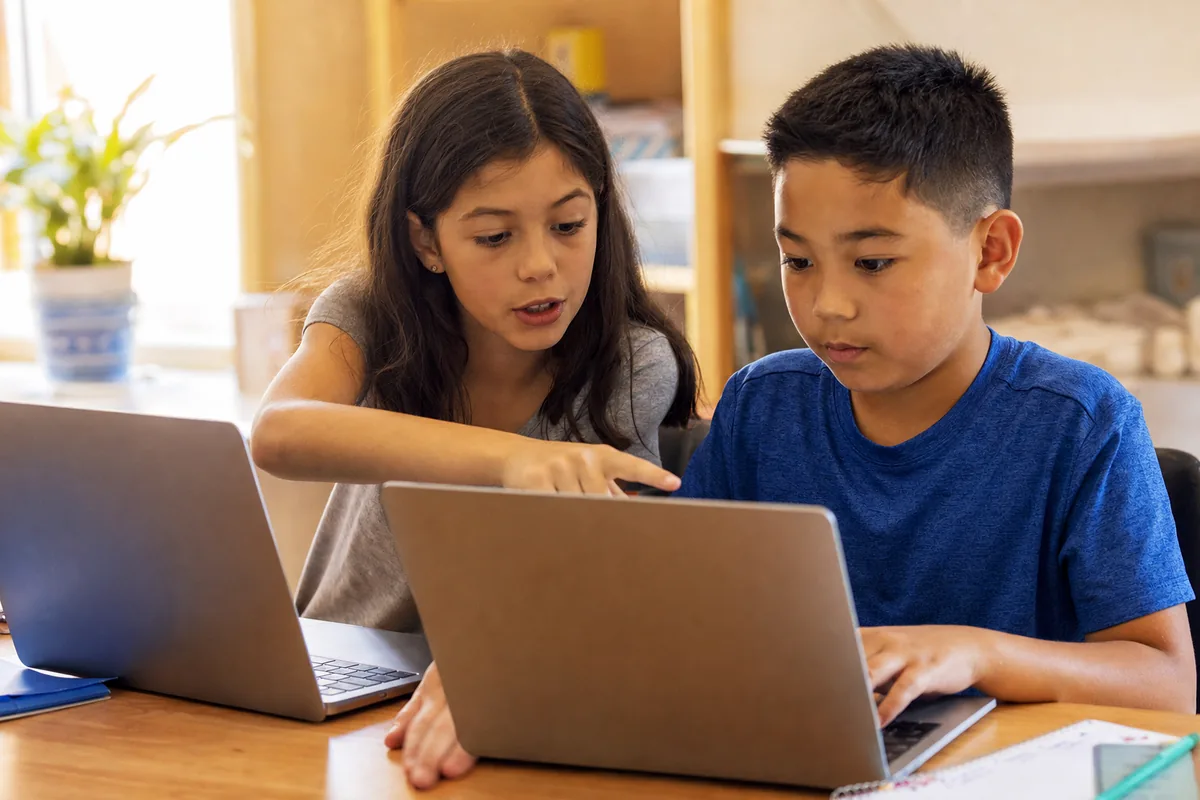 Two children teaching each other while working on laptops with AI